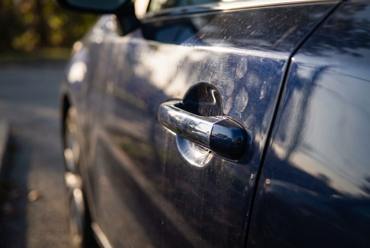 Close view of fresh fingerprints and light dust around a car door handle.